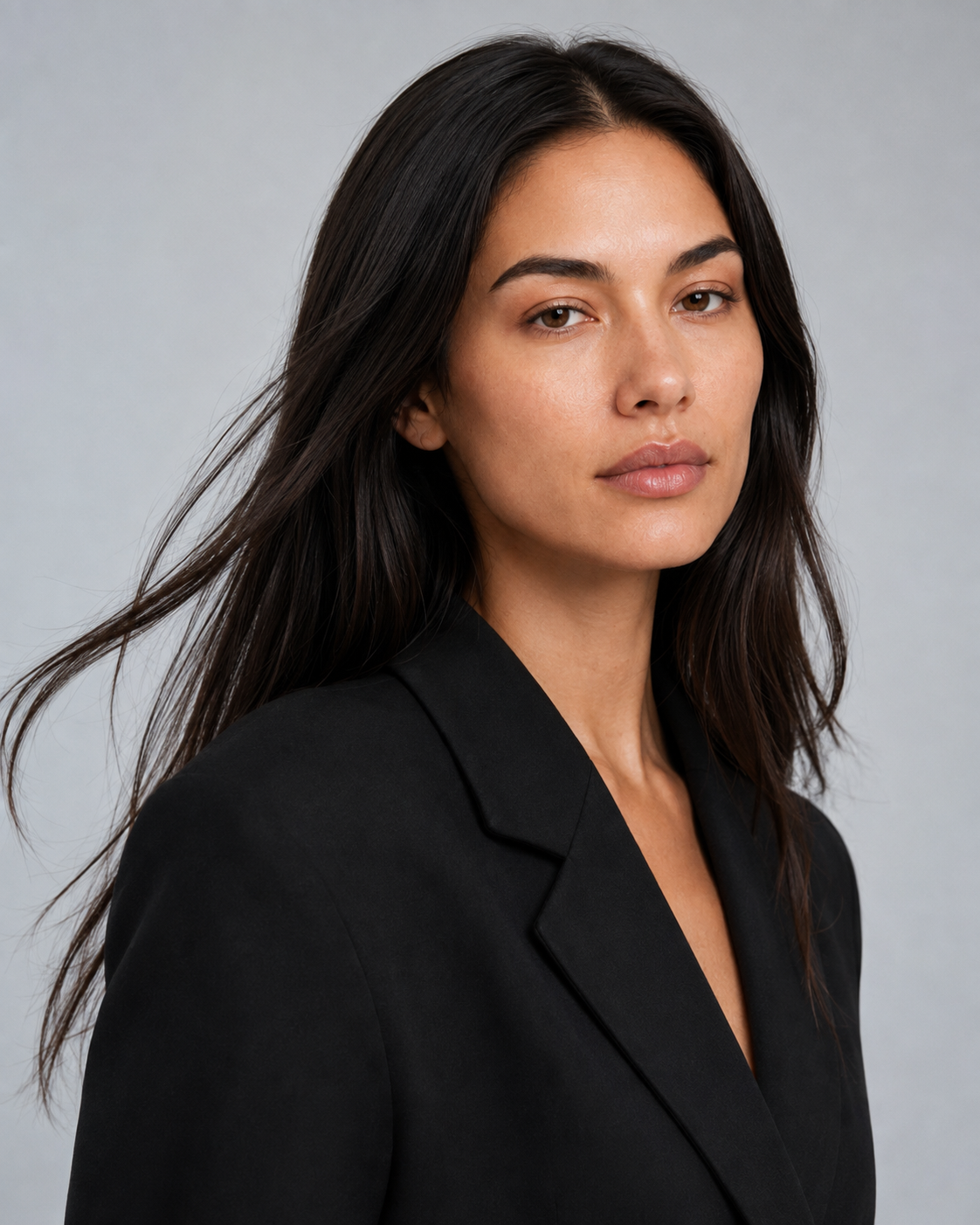 Su wearing a black blazer against a neutral grey studio background.
